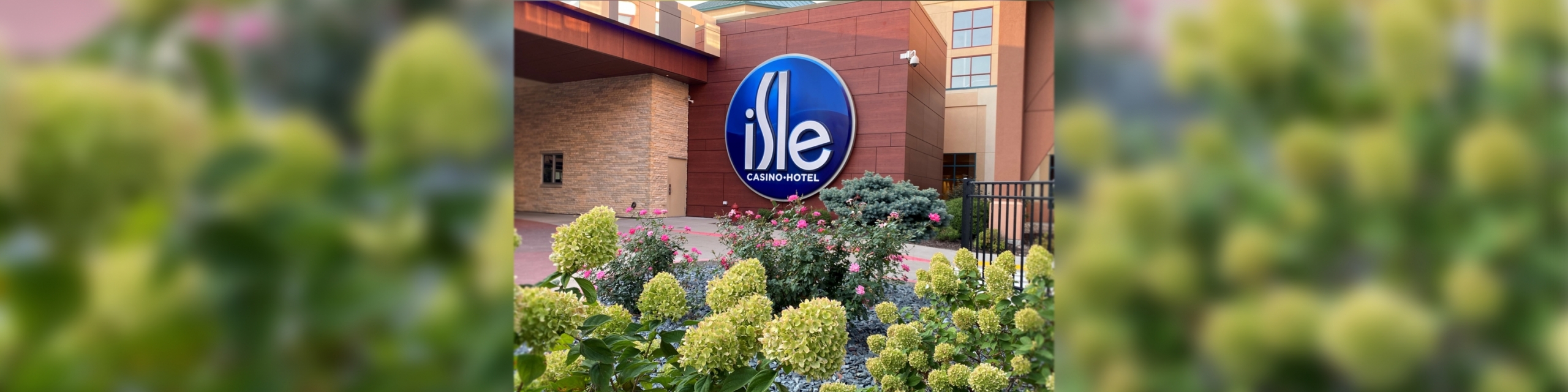 Isle Casino landscaping, with bushes in light and dark green, purple and pink flowers, and the Isle sign hangs on the brick wall in the background.